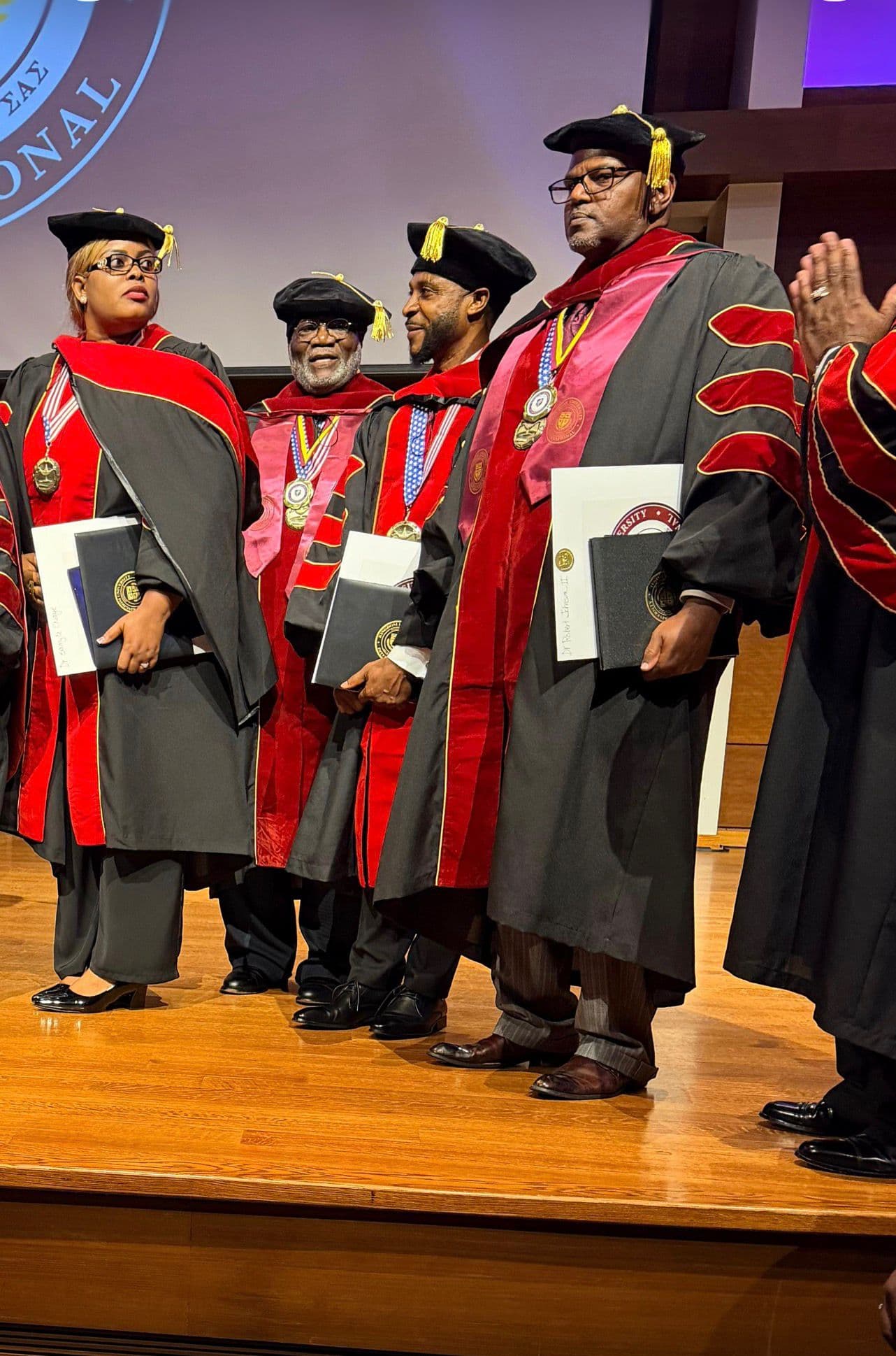 Graduates in red and black robes holding diplomas